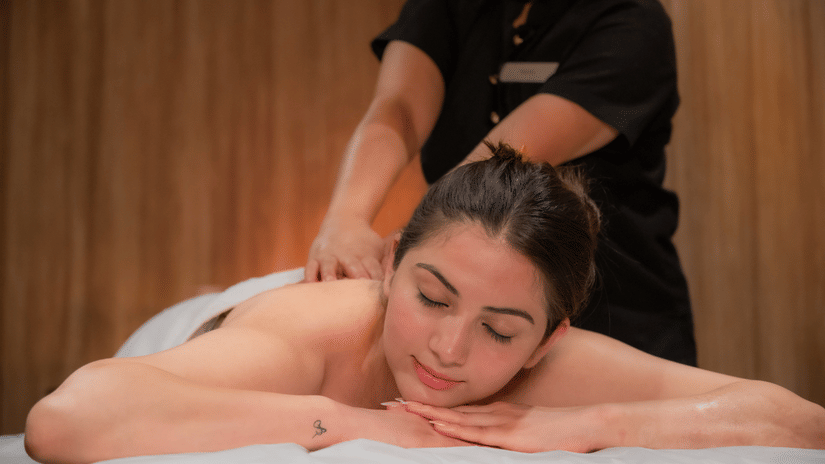 A women lying on her stomach and receiving back massage by a masseuse wearing a black uniform at The Manor Luxury Apartments, Shimla.